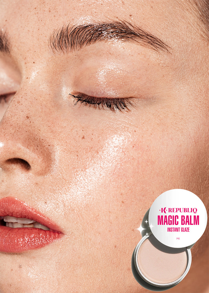 A close-up of a person's face with their eyes closed, showing dewy, glowing skin and freckles. In the bottom right corner, a K Republiq Magic Balm Instant Glaze product is shown with its lid partially open, next to the person's face.